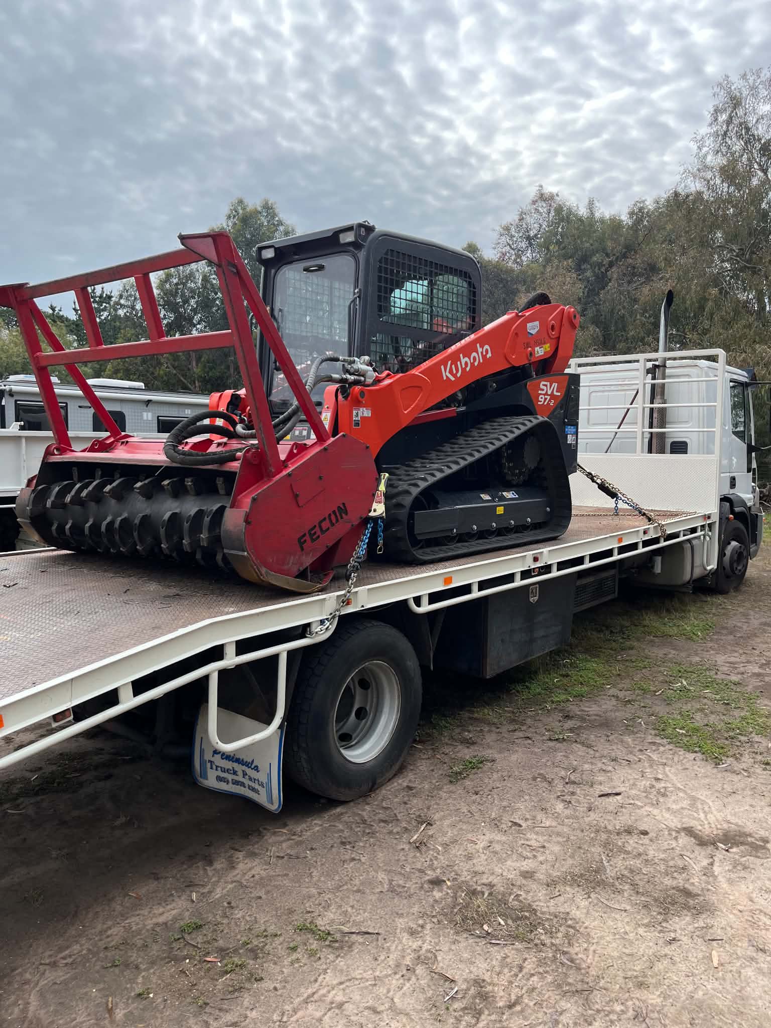 Kubota skid steer and Fecon forestry mulcher secured on the beavertail truck